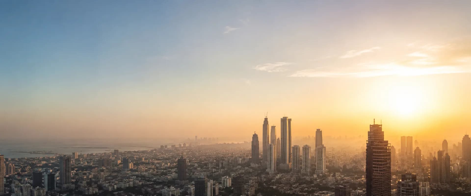 The Mumbai skyline at sunrise, city towers emerging from morning haze with the sun low on the horizon
