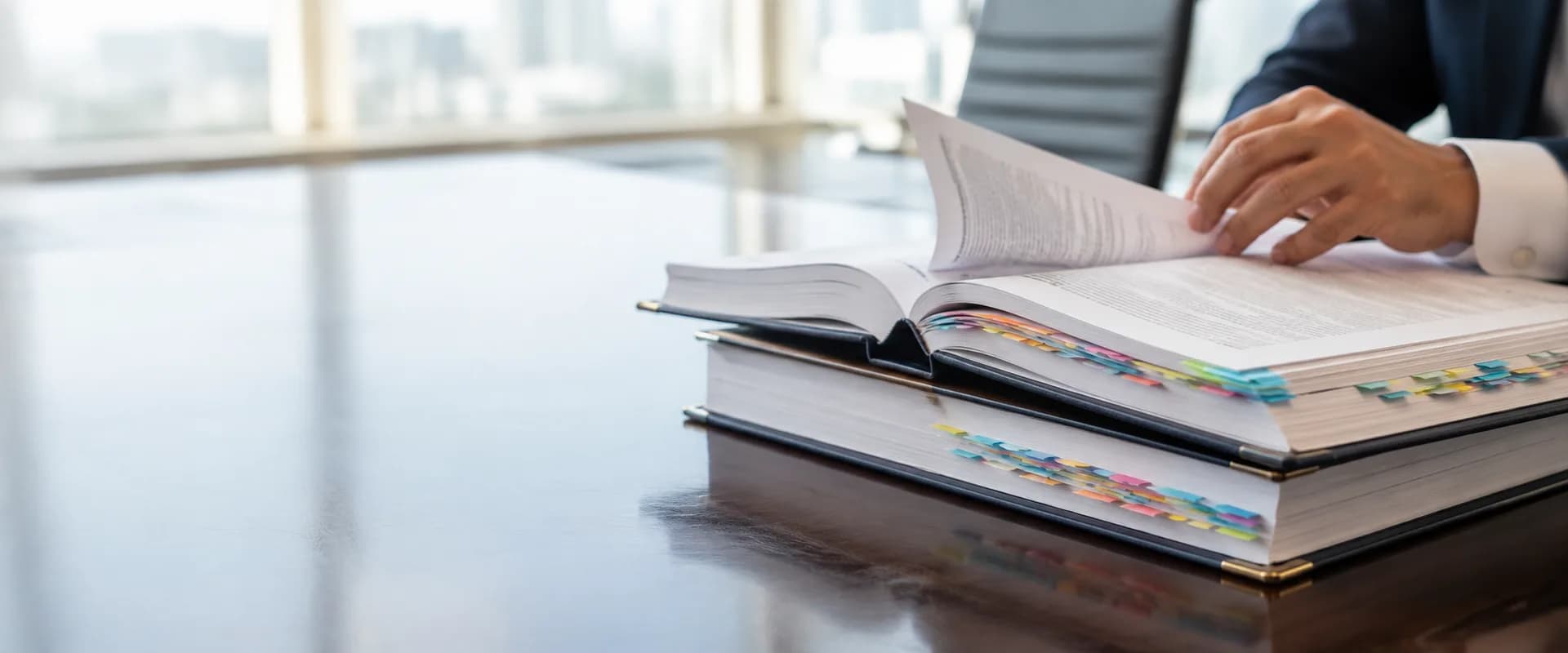 Hands turning the page of a thick tabbed prospectus volume on a polished boardroom table