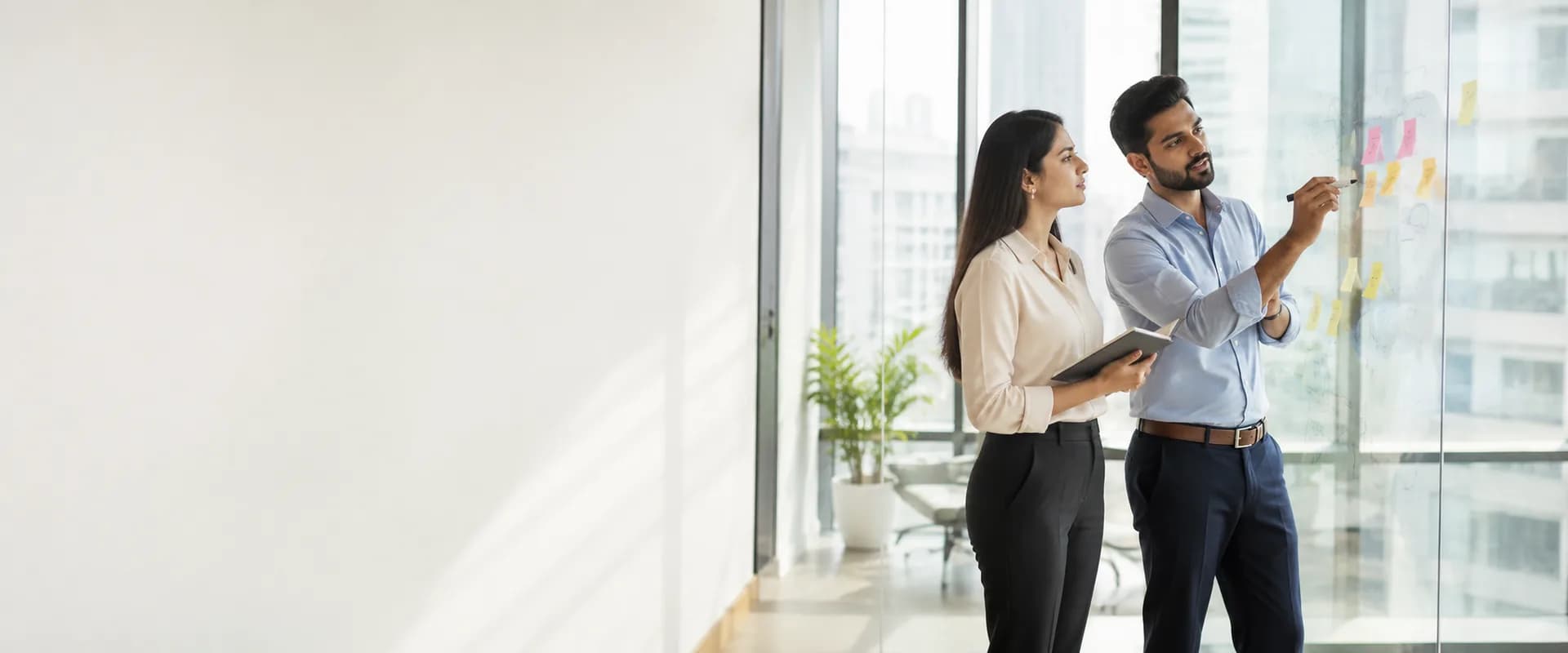 Two advisors mapping a growth plan in marker and sticky notes on a glass wall in a sunlit office