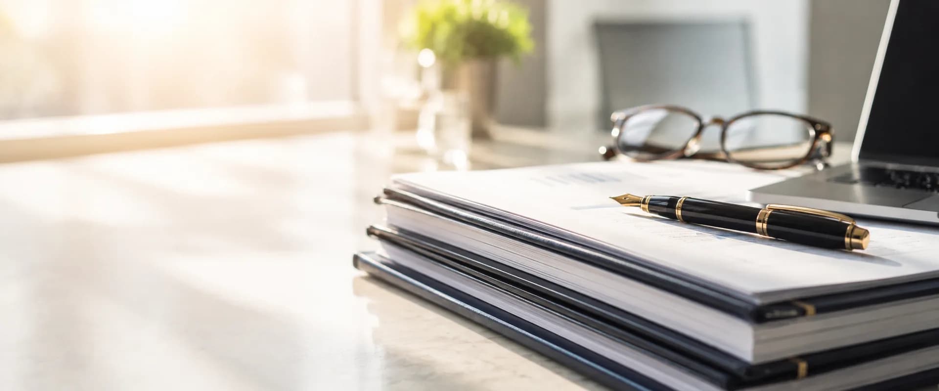A fountain pen resting on a stack of bound financial documents on a sunlit desk
